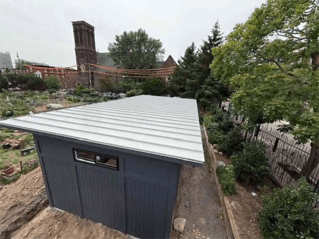 Aerial view of a newly built dark navy accessory structure with a standing-seam metal roof in an urban community garden